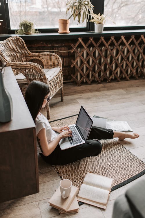 Брюнетка с ноутбуком сидит на полу в комнате и работает в интернете
