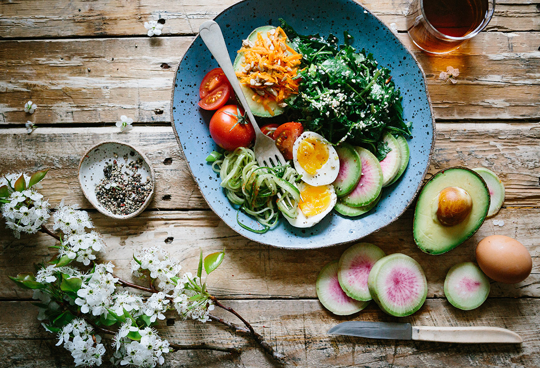 Тарелка с салатом, чашка с чаем, цветы и овощи на деревянной  поверхности